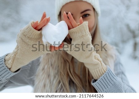 Close-up girl holds a snowy heart in front of her in gloves Royalty-Free Stock Photo #2117644526