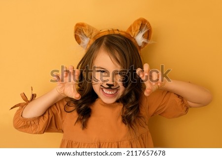 A curly-haired brunette girl with a tiger's rim and ears and a painted face growls, showing her teeth and making a gesture with her hands. The Year of the Tiger according to the Eastern calendar