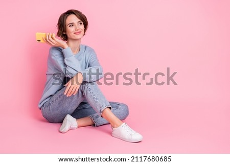 Full body photo of minded pretty person sit floor hold gadget look empty space isolated on pink color background
