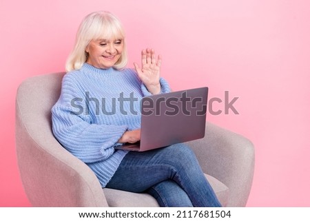 Portrait of attractive cheerful grey-haired woman using laptop calling waving hi hello isolated over pink pastel color background