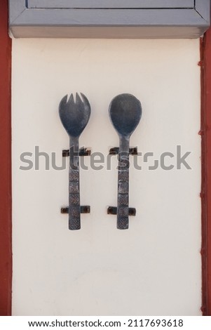 Large metal and old spoon and fork with carvings and patterns on them hang on the wall of cafe or restaurant on Santorini island, Oia, Greece. Signboard on the street