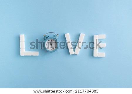 Love letters made of sugar cubes and alarm clock. Valentine's day card idea. Minimal concept. Blue background.