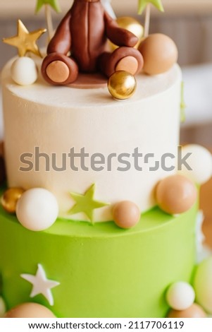 part of two-tiered white-green cake with balls, stars and a teddy bear on the table for a children's holiday. the tradition of baking a birthday cake. professional confectioner.