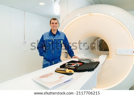 installer engineer of the magnetic resonance imaging with tools apparatus near the scanner. professional services. sale and service of medical equipment. blue uniform Royalty-Free Stock Photo #2117706215
