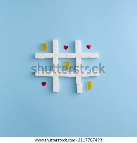 Valentine day composition. Tic tac toe with gummy bear and heart. Sugar cubes. Blue background. 
