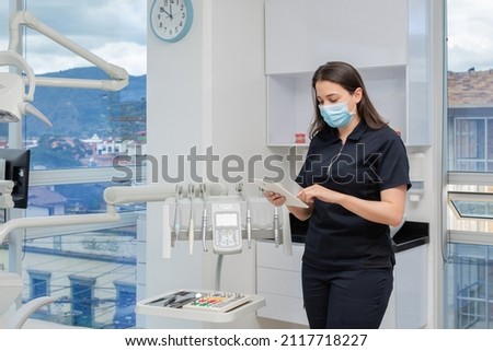 Dentist woman next to dental clinic equipment holding a tablet. Dental clinic concept Royalty-Free Stock Photo #2117718227