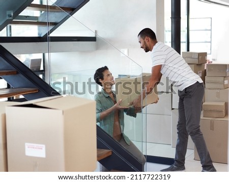 They make moving house look easy. Shot of a happy young couple passing boxes to each other while moving into their new home. Royalty-Free Stock Photo #2117722319