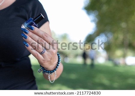 Woman's beautiful hand with long nails and blue manicure with bottles of nail polish	