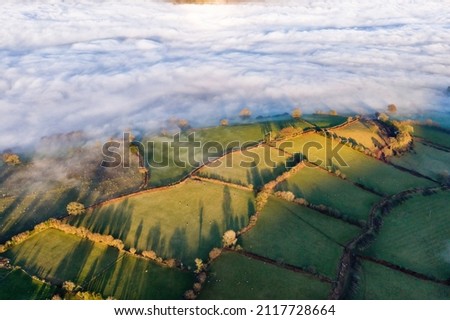 Aerial view of a fog filled valley surrounded by rural farmland in afternoon sunshine (Brecon Beacons, Wales, UK) Royalty-Free Stock Photo #2117728664