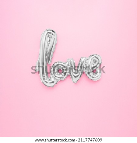 The word LOVE made of a shiny helium balloon on a pastel pink background.Minimal love concept. Flat lay, top view