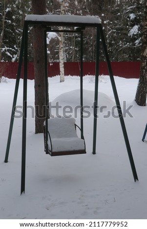 Snow-covered green iron swing in the country
