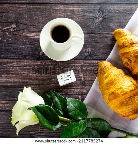A white rose flower, croissants, a coffee cup on the background of a wooden table with the recognition "I love you".  Top view. romantic coffee.