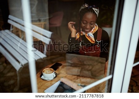 A smart African college girl sits in the cafeteria and studies for an exam. The picture was taken from the outside. A girl on student exchange sitting in a coffee shop and studying.