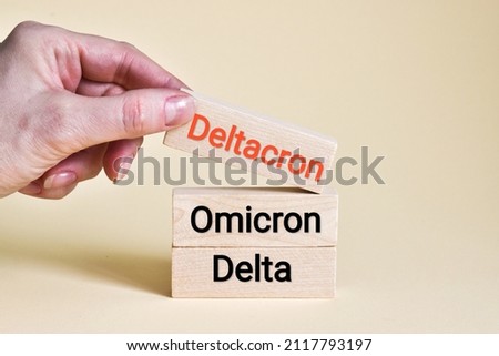Deltacron, omicron, delta text on wooden blocks. A hand moves a wooden block with the word DELTACRON on a beige background. Medical and delta or micron variant concept. Copy space