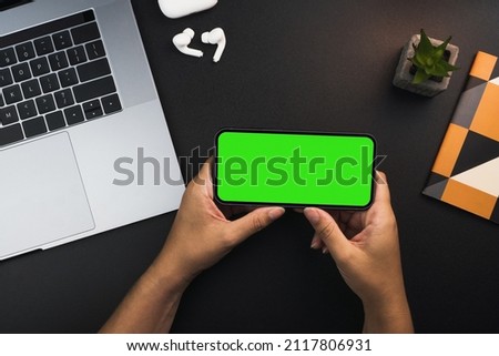 Girl holding a smartphone with green screen on black background table. Office environment. Chroma Key.