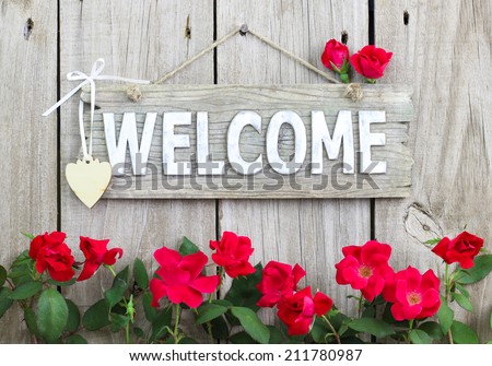 Weathered welcome sign hanging on rustic wood fence with flower border of red roses