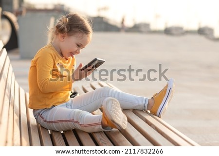 Cute child using smartphone and smiling outside in urban park. Video call family friends. Online. internet fun website for children. New generation and modern tech overuse, parental control concept