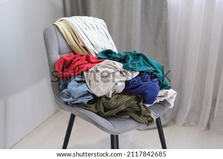 person throws used clothes on the chair. Pile clothes on chair. Heap of used clothes for donation and recycling. Royalty-Free Stock Photo #2117842685