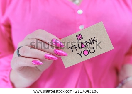 Female hands with long nails and neon pink nail polish hold a picture with the inscription Thank you
