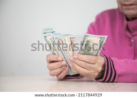 Senior income concept. An elderly woman at the table counts cash dollars. Close-up. Selective focus on hand and dollars