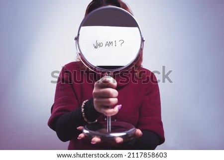 caucasian woman holds a mirror in her hand with the iscription who am i on white background Royalty-Free Stock Photo #2117858603