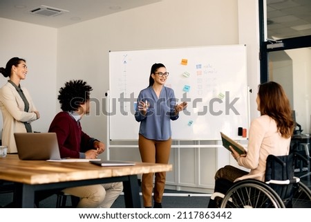 Happy entrepreneur talking to her coworkers about inclusive business strategy while holding presentation in the office. Royalty-Free Stock Photo #2117863442