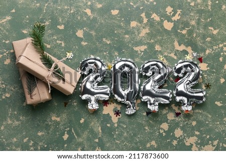 Silver balloons in shape of figure 2022 and Christmas presents on color background