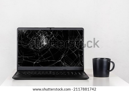 a laptop with a broken screen and a black mug of tea on a table against a white wall