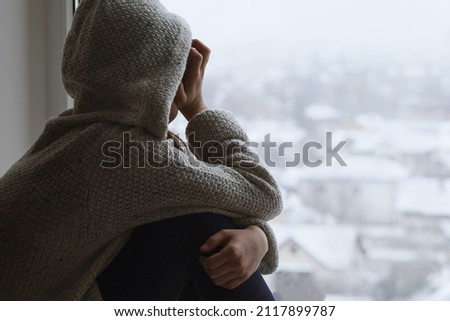 Depressed Upset sad teen girl looks out the window back to the camera. Difficult teenage maturation. Negative thoughts in teen. Children need help Royalty-Free Stock Photo #2117899787