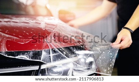 Process of pasting hood of red car with protective vinyl film from gravel chips and scratches. Transparent protection for paint. Royalty-Free Stock Photo #2117906813