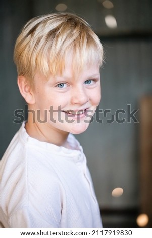 Cute blonde pre-teen boy with relaxed pose sitting in rustic outdoor county setting