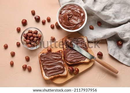 Wooden board of bread with chocolate paste and hazelnuts on beige background