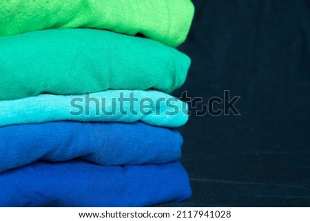 A stack of multicolored fabric in cool colors. Background with folded blue and green clothes with empty space for information. T-shirts of different colors