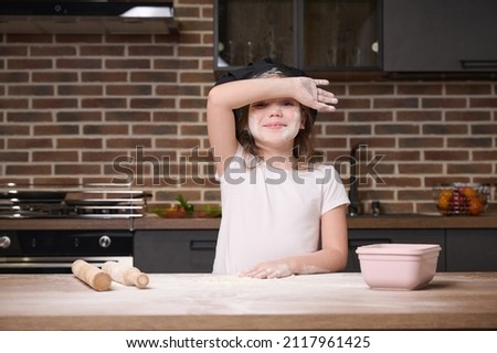 Little girl having fun cooking at the kitchen table. 