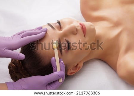 Beautician is removing hair from beautiful female face with hot wax. Woman has a beauty treament procedure. Depilation, epilation, skin and health care concepts. Royalty-Free Stock Photo #2117963306