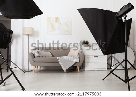 Set of stylish furniture surrounded by professional lighting equipment in photo studio. Cozy living room interior imitation