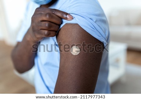 African man holding up his shirt sleeve and showing his arm with bandage after receiving vaccination. covid 19 immunization