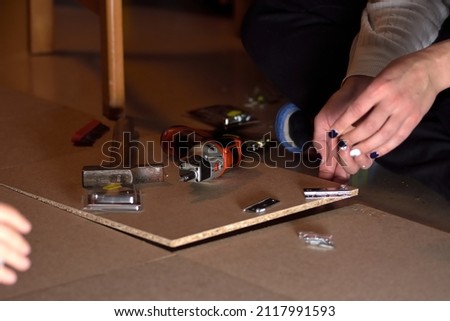 a young woman with painted fingernails sitting on the floor doing DIY at home, using a hammer, a battery-powered screwdriver and wood. selective focus