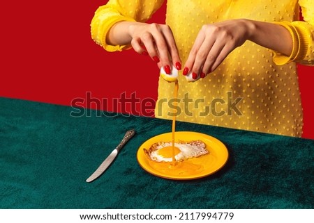 Woman cooking fried eggs on plate isolated on green and red background. Vintage, retro style interior. Food pop art photography. Complementary colors, red, green and yellow. Copy space for ad, text