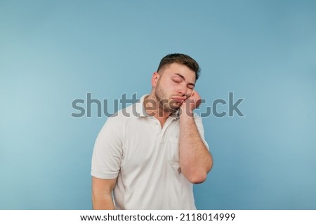 Tired man with bristles and in a white T-shirt sleeps on his arm on a blue background. Isolated