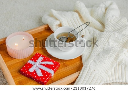 Valentine's day concept. Festive decor details. Candle, Red gift box with a bow and a mug of hot tea on a wooden tray.