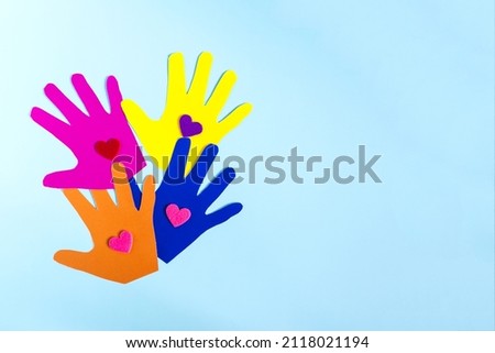 Abstract background colored paper depicting children's hands with colored hearts on a light background.
