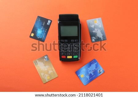 New modern payment terminal and credit cards on orange background, flat lay