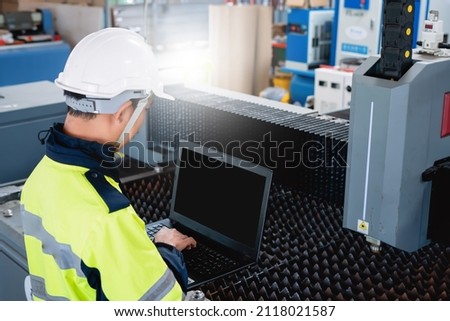 Factory mechanical engineer wearing green work clothes and protective pieces uses laptop to show gestures working in an industrial factory.