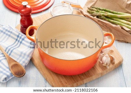 Orange dutch oven on wooden board with ingredients around it Royalty-Free Stock Photo #2118022106