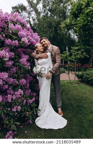 Walk of the bride and groom in the summer park. The bride hugs the groom. Photo on a background of pink flowers. Newlyweds in seclusion.