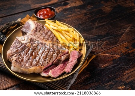 Roast Italian Florentine or porterhouse beef meat Steak in a plate with french fries. Wooden background. Top view. Copy space Royalty-Free Stock Photo #2118036866