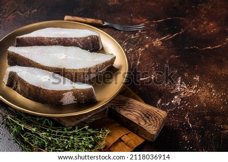 Sliced halibut fish, raw steaks on plate with thyme. Dark background. Top view. Copy space
