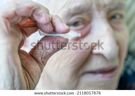 eyedrops, closeup wrinkled hand of old senior woman or man holding single use natural tear or eyedrops with selective focus. applying medicinal drops for eyesight. old people health care photo