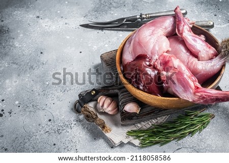 Raw hare game meat, legs and offals in wooden plate with herb. Gray background. Top view. Copy space